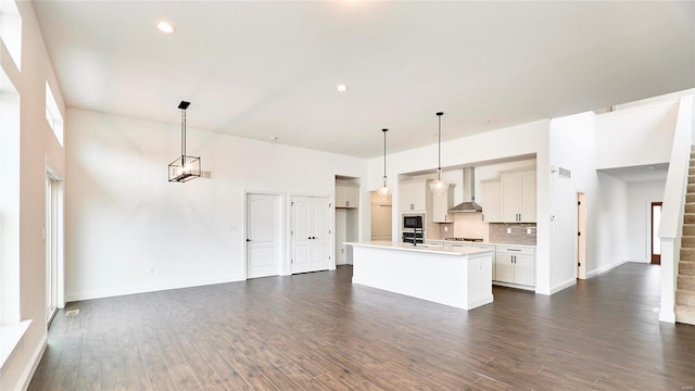 kitchen with dark wood-type flooring, a center island with sink, decorative light fixtures, and wall chimney range hood