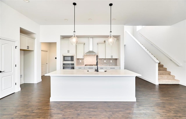 kitchen with hanging light fixtures, backsplash, dark hardwood / wood-style floors, a kitchen island with sink, and wall chimney range hood