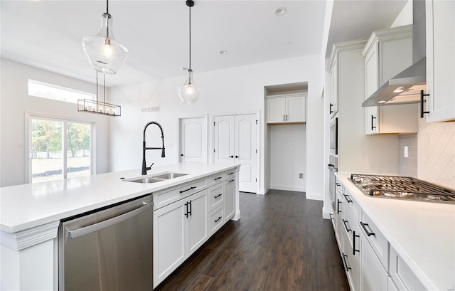 kitchen featuring pendant lighting, tasteful backsplash, wall chimney range hood, stainless steel appliances, and a kitchen island with sink