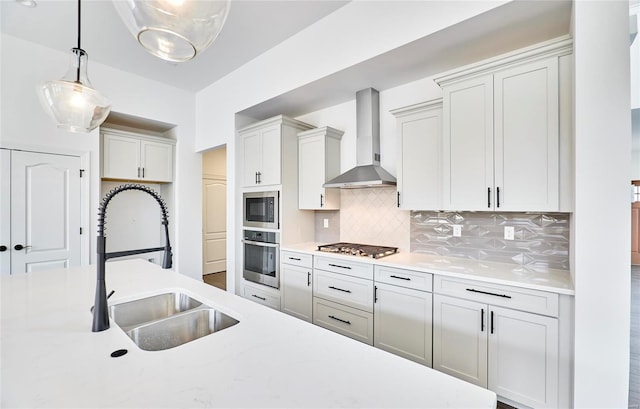 kitchen featuring pendant lighting, sink, backsplash, stainless steel appliances, and wall chimney range hood