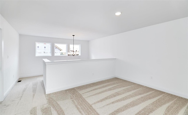 unfurnished room featuring a notable chandelier and light carpet