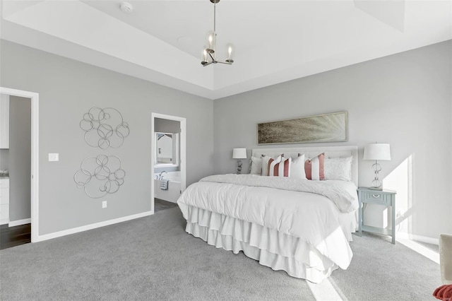 carpeted bedroom featuring an inviting chandelier, ensuite bathroom, and a tray ceiling