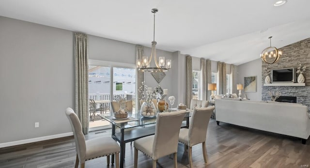 dining area with an inviting chandelier, dark hardwood / wood-style flooring, a fireplace, and vaulted ceiling