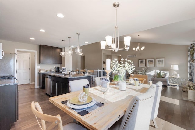 dining space with an inviting chandelier, wood-type flooring, sink, and lofted ceiling