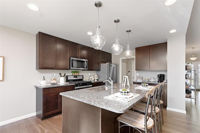 kitchen with a breakfast bar, stainless steel appliances, light hardwood / wood-style floors, and decorative light fixtures