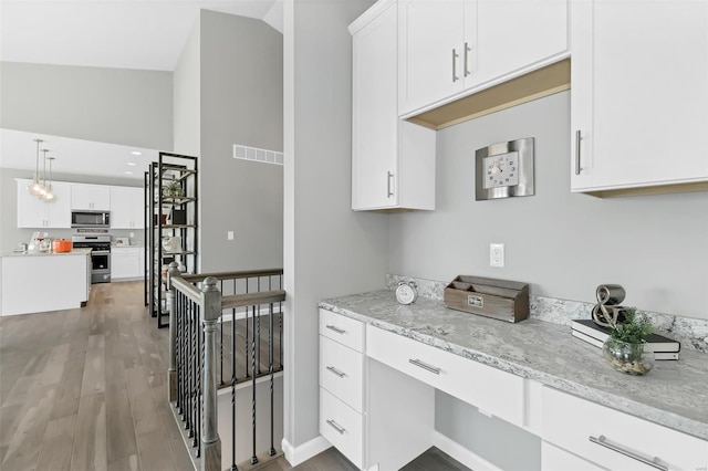 kitchen with stove, light stone countertops, decorative light fixtures, white cabinetry, and light wood-type flooring