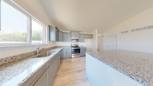 kitchen with lofted ceiling, appliances with stainless steel finishes, gray cabinets, sink, and light stone counters