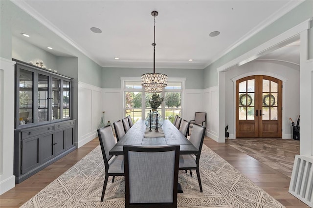 dining room featuring a notable chandelier, light wood-type flooring, ornamental molding, and french doors