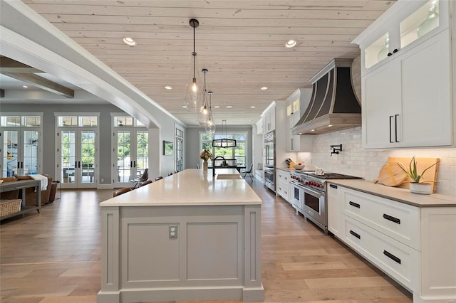 kitchen featuring a center island with sink, custom exhaust hood, french doors, and stainless steel appliances