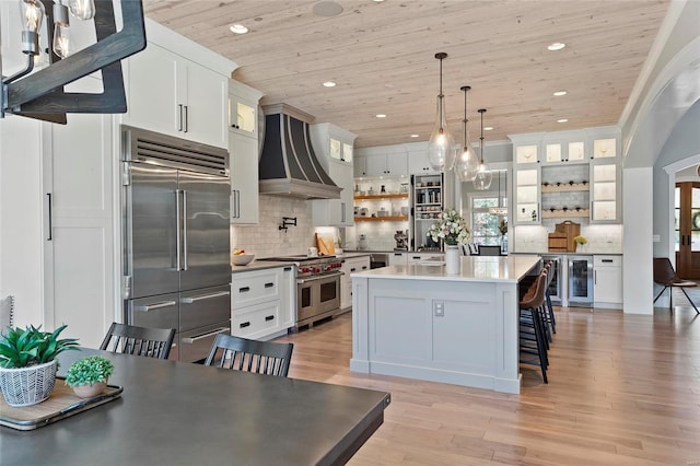 kitchen featuring custom range hood, premium appliances, white cabinets, and a breakfast bar