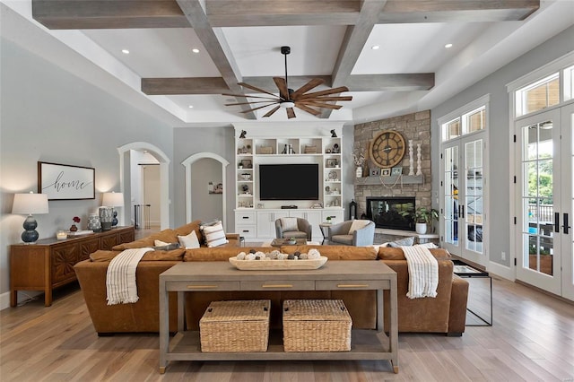 living room featuring light wood-type flooring, a stone fireplace, coffered ceiling, and french doors