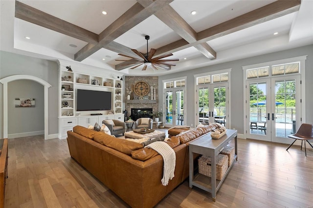 living room featuring beamed ceiling, coffered ceiling, a fireplace, light hardwood / wood-style floors, and french doors