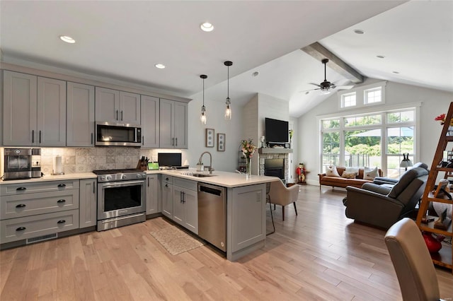 kitchen with appliances with stainless steel finishes, light hardwood / wood-style floors, kitchen peninsula, a fireplace, and lofted ceiling with beams