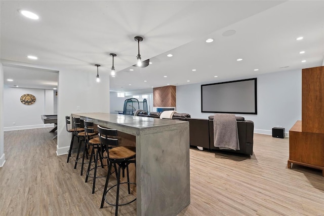 kitchen with a kitchen breakfast bar, a kitchen island with sink, light wood-type flooring, and decorative light fixtures