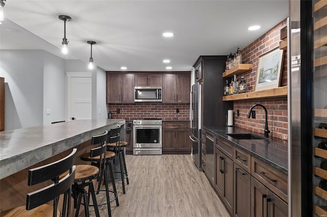 kitchen with sink, light wood-type flooring, stainless steel appliances, dark brown cabinetry, and pendant lighting