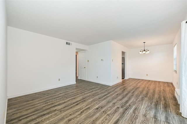 spare room featuring dark wood-type flooring and a chandelier