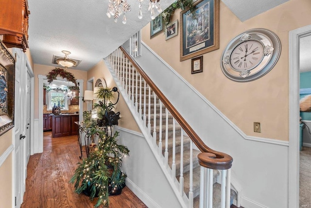 stairway featuring an inviting chandelier, a textured ceiling, and dark hardwood / wood-style floors