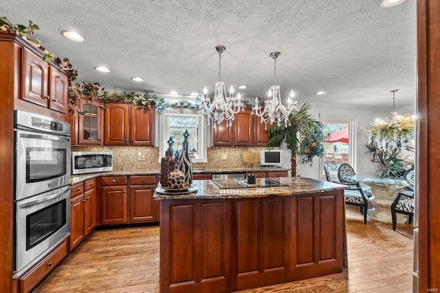 kitchen with hanging light fixtures, an inviting chandelier, light hardwood / wood-style floors, an island with sink, and stainless steel appliances