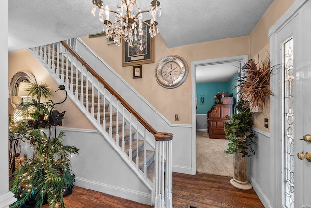 foyer entrance featuring an inviting chandelier, dark carpet, and a textured ceiling