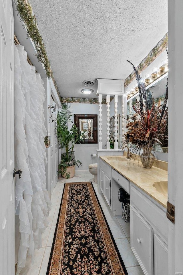 bathroom featuring tile floors, toilet, double vanity, and a textured ceiling