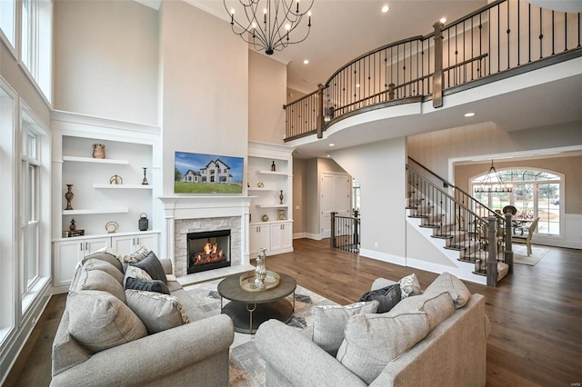 living room featuring a towering ceiling, dark wood-type flooring, built in features, and a stone fireplace