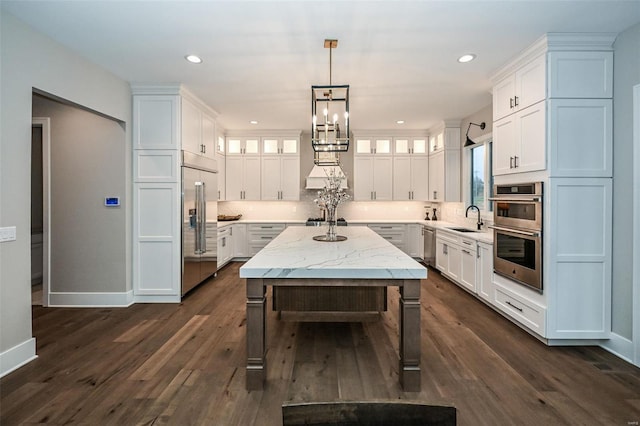 kitchen with stainless steel appliances, light stone countertops, a kitchen island, sink, and white cabinetry