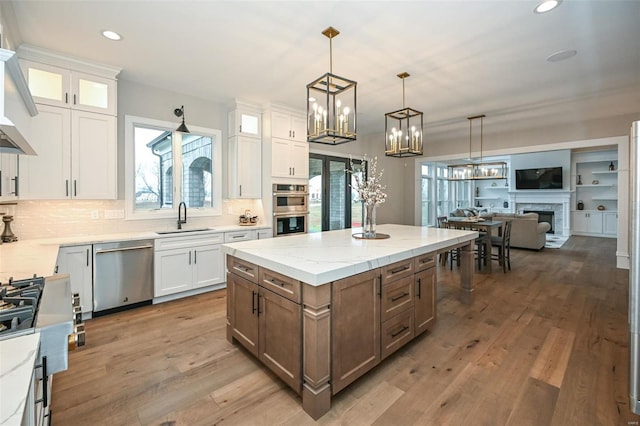 kitchen with stainless steel appliances, hanging light fixtures, a kitchen island, white cabinets, and sink