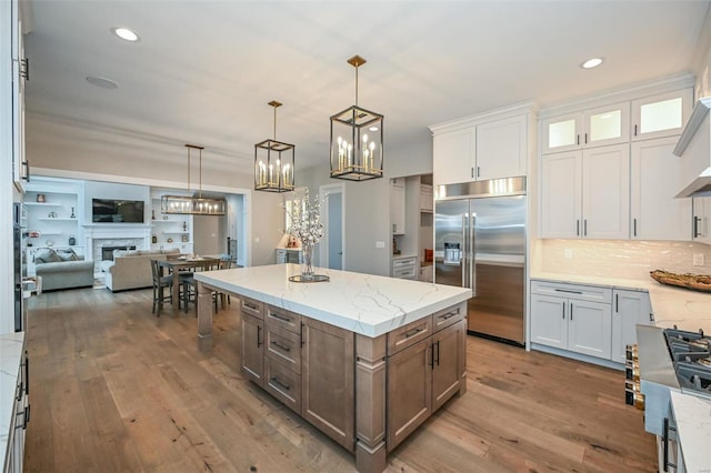 kitchen featuring stainless steel built in refrigerator, white cabinets, light stone counters, and hanging light fixtures