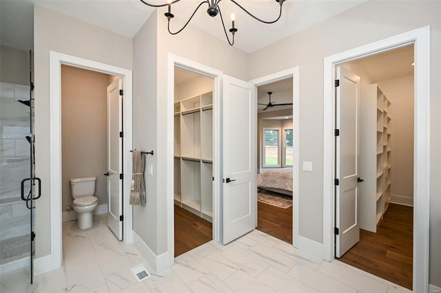 bathroom featuring a shower with door, ceiling fan with notable chandelier, and toilet