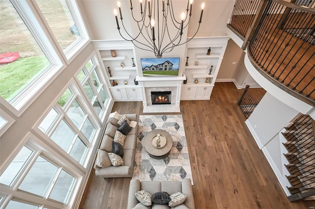 living room with a chandelier, a towering ceiling, a fireplace, and wood-type flooring