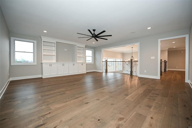 unfurnished living room featuring ceiling fan with notable chandelier, built in shelves, and hardwood / wood-style flooring