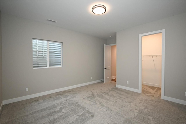 unfurnished bedroom featuring a walk in closet, a closet, and light colored carpet