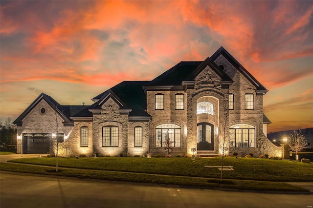 french country style house with a garage, a front yard, concrete driveway, and brick siding