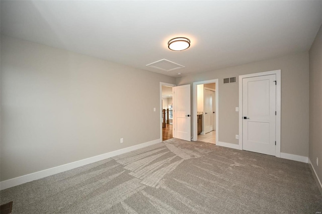 unfurnished bedroom with light carpet, attic access, visible vents, baseboards, and ensuite bath