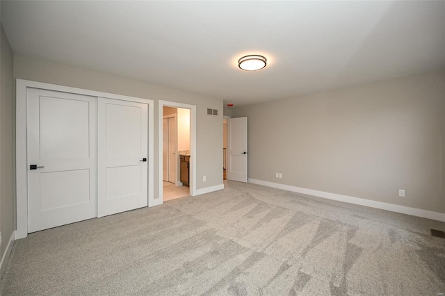 unfurnished bedroom featuring a closet, light colored carpet, visible vents, ensuite bathroom, and baseboards