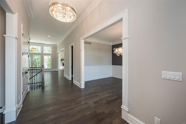 hall with dark wood-style flooring, crown molding, a decorative wall, a notable chandelier, and an upstairs landing