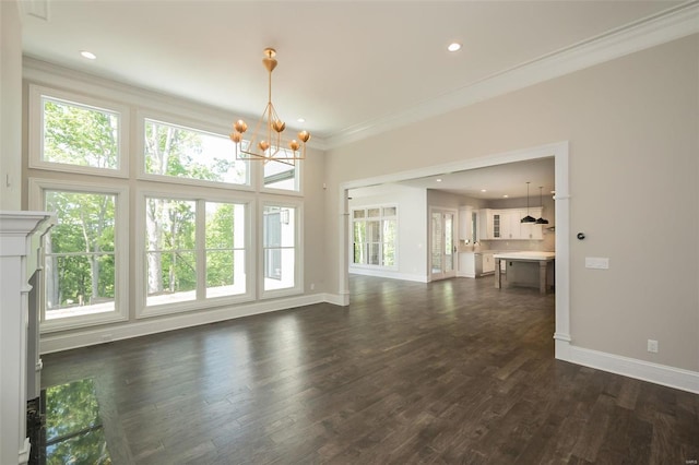 unfurnished living room with dark wood finished floors, crown molding, baseboards, and an inviting chandelier