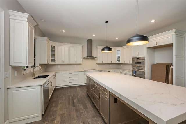 kitchen featuring a sink, stainless steel appliances, white cabinets, wall chimney range hood, and a center island