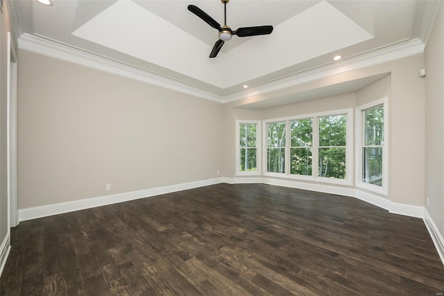 spare room with a raised ceiling, dark wood-style floors, baseboards, and ornamental molding