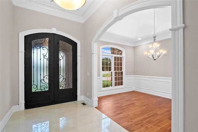 tiled foyer featuring french doors, an inviting chandelier, and ornamental molding