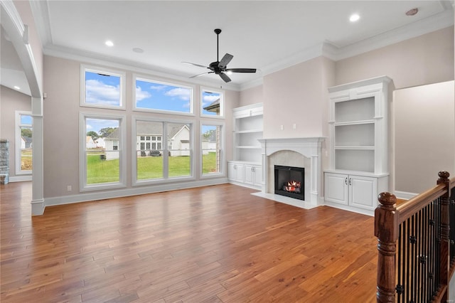 unfurnished living room with ceiling fan, built in features, light hardwood / wood-style flooring, and crown molding