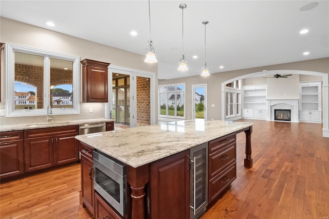 kitchen with appliances with stainless steel finishes, hanging light fixtures, ceiling fan, backsplash, and light hardwood / wood-style floors