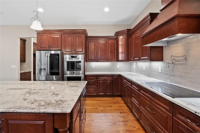 kitchen with pendant lighting, tasteful backsplash, appliances with stainless steel finishes, custom range hood, and light wood-type flooring