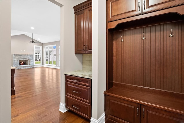 mudroom with ceiling fan, lofted ceiling, a stone fireplace, and hardwood / wood-style floors