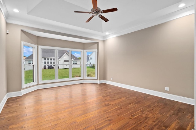 empty room with a raised ceiling, ceiling fan, and light wood-type flooring