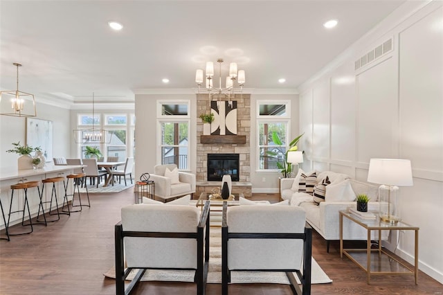 living room featuring dark wood-type flooring, crown molding, a stone fireplace, and a chandelier