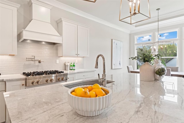 kitchen with white cabinetry, hanging light fixtures, light stone countertops, stainless steel gas cooktop, and custom exhaust hood