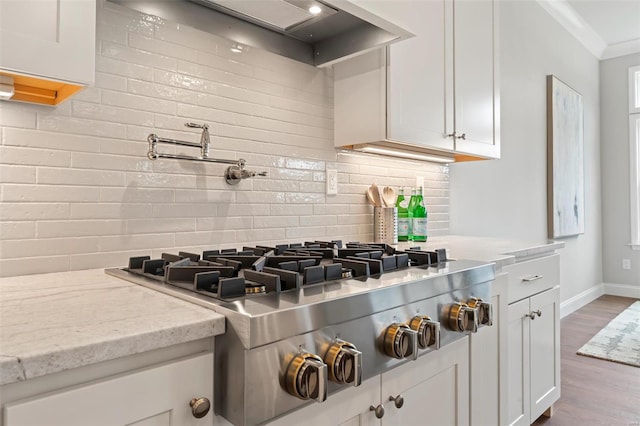 kitchen with stainless steel gas stovetop, tasteful backsplash, white cabinetry, light stone countertops, and wall chimney exhaust hood