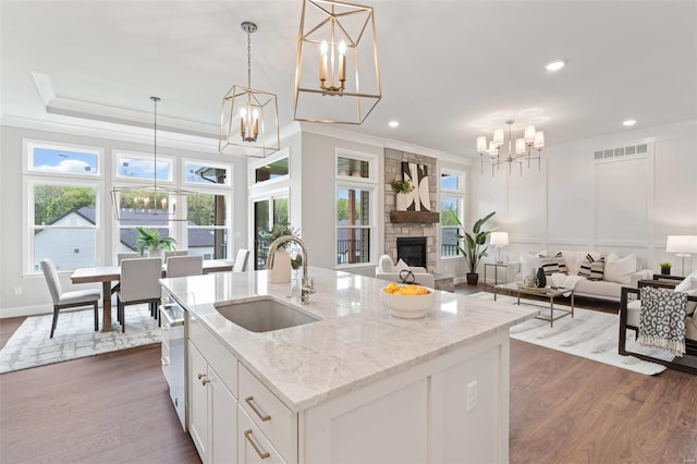 kitchen with sink, an inviting chandelier, a kitchen island with sink, white cabinets, and decorative light fixtures