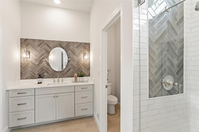 bathroom featuring tile patterned flooring, vanity, toilet, and tiled shower